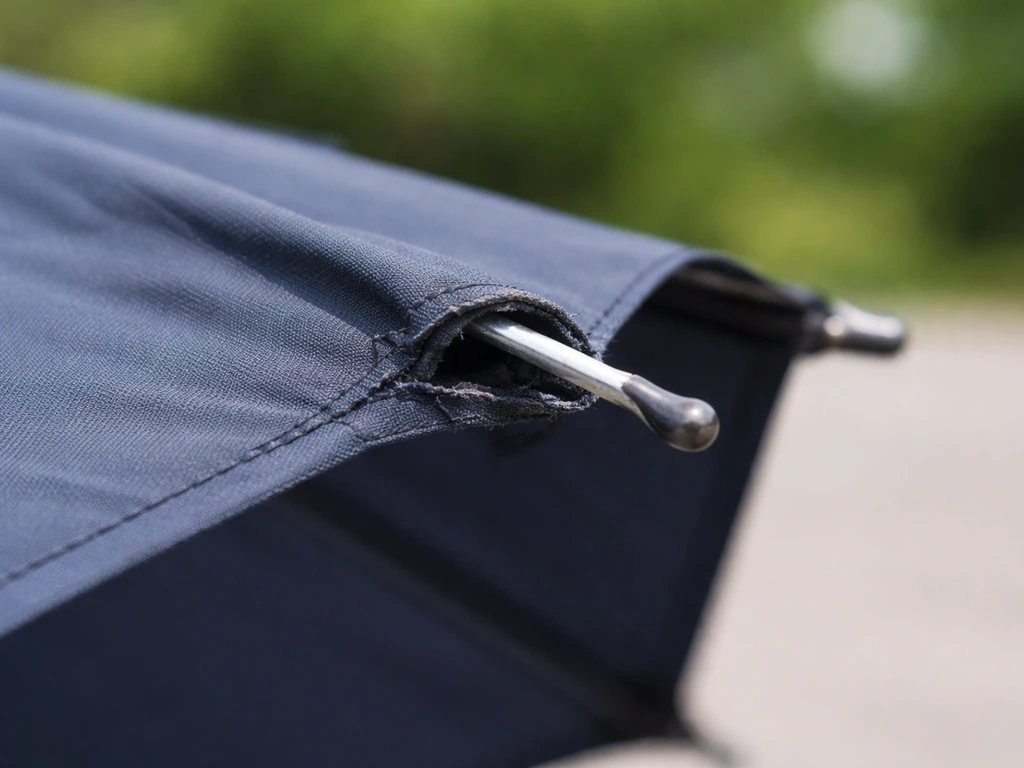 Close-up view of an umbrella rib torn through the canopy hem near the tip, showing a loose frame.